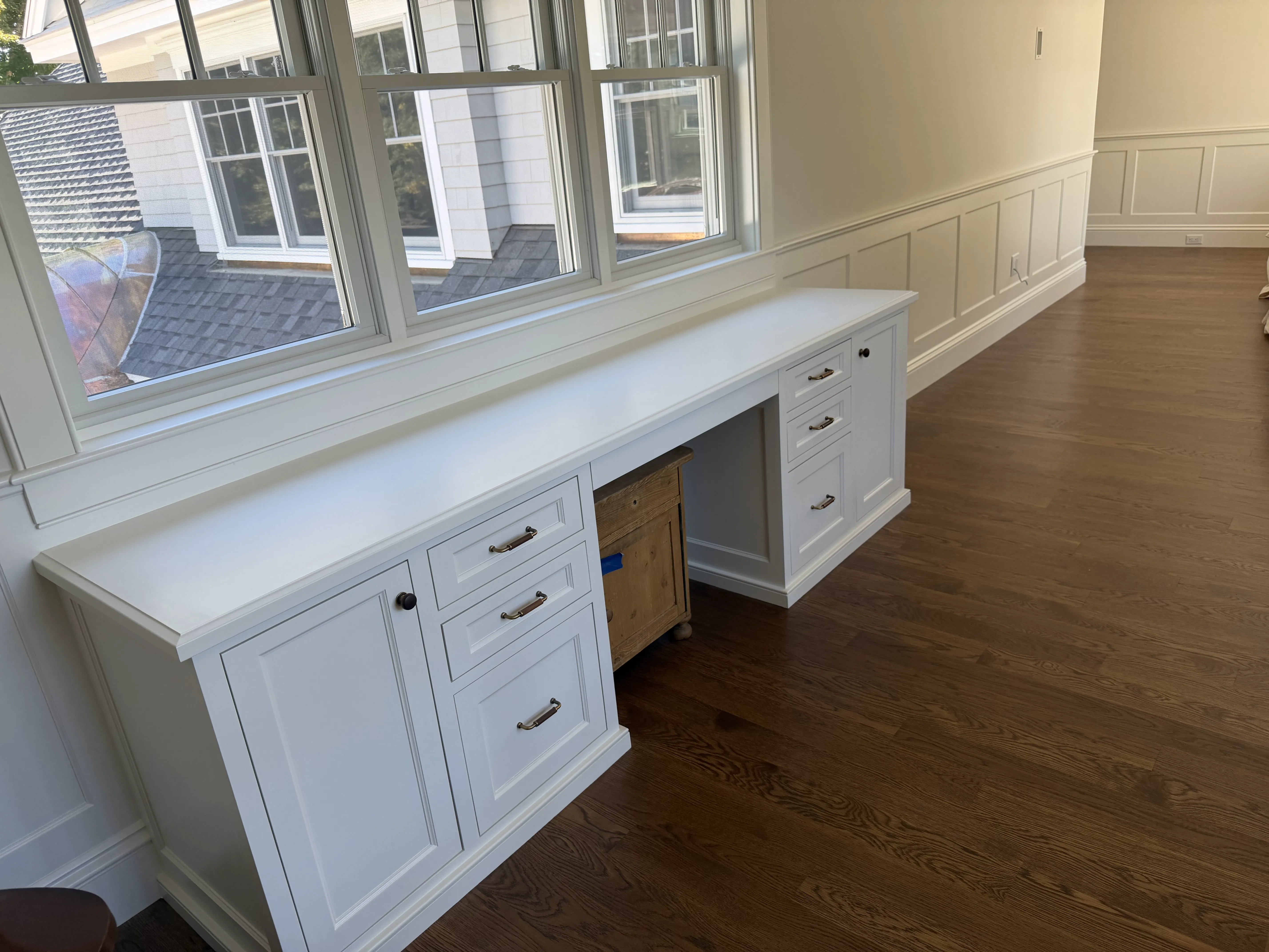 White fitted desk and drawer cabinets beneath windows, with paneled wall trim