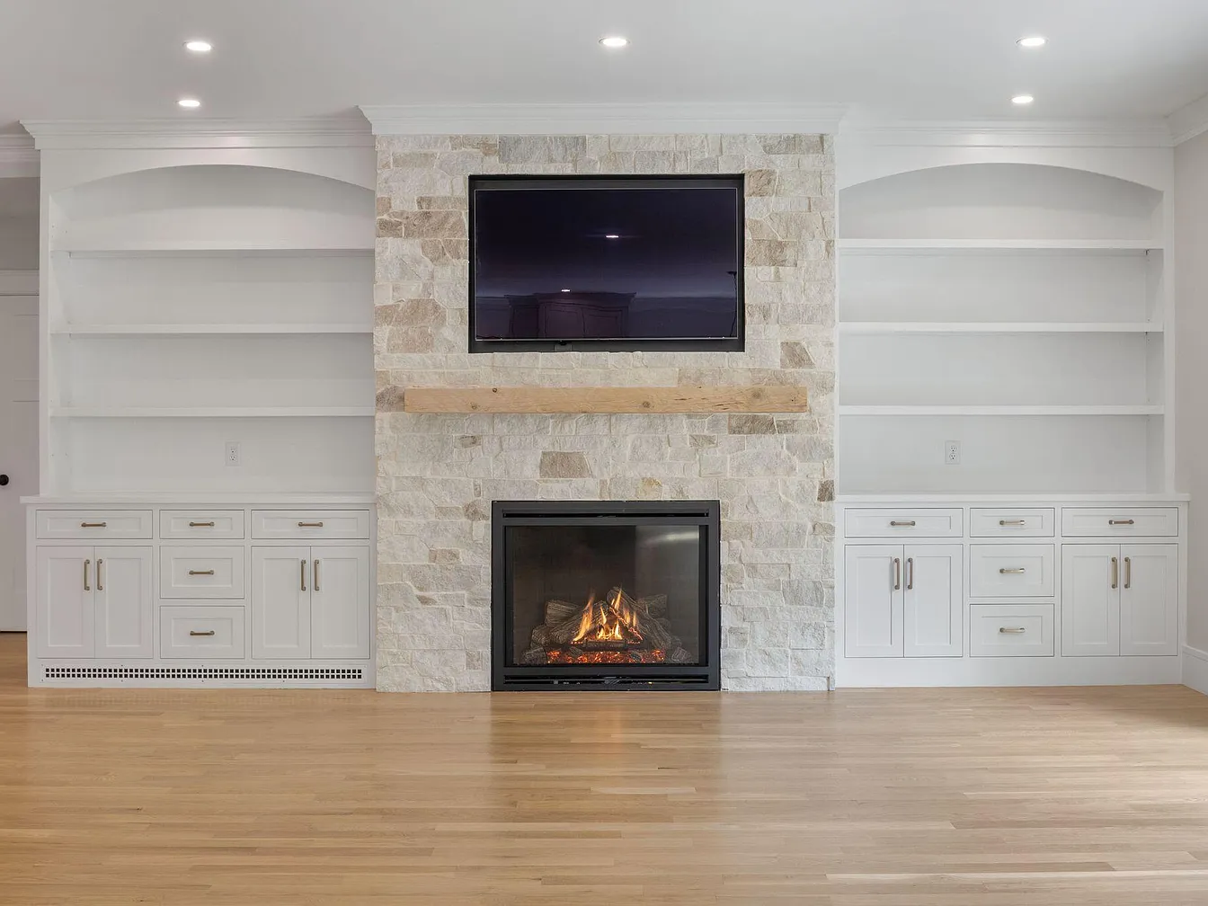 White arched bookcases and paneled base cabinets framing a stone fireplace
