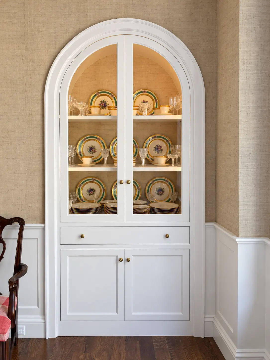 White arched display cabinet with glazed doors, lit shelves, a drawer and paneled base storage