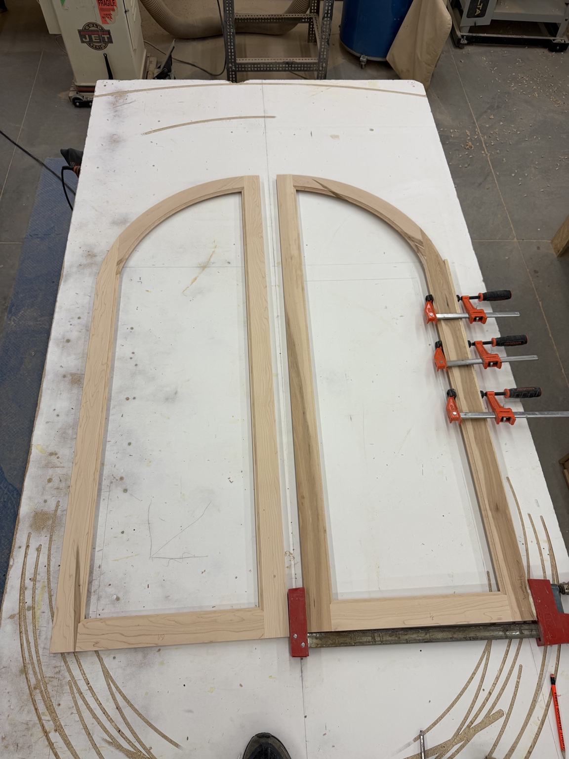 Two tall curved wood frames on a layout table with clamps along one frame