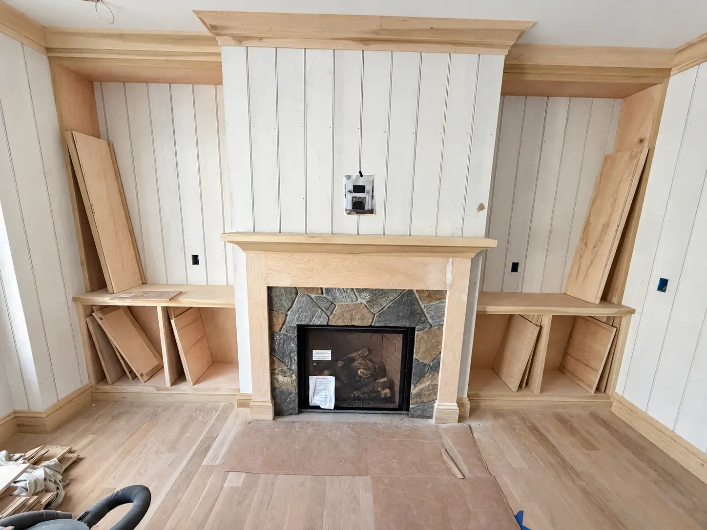 Unfinished wood fireplace surround with fitted cabinets and paneling during installation
