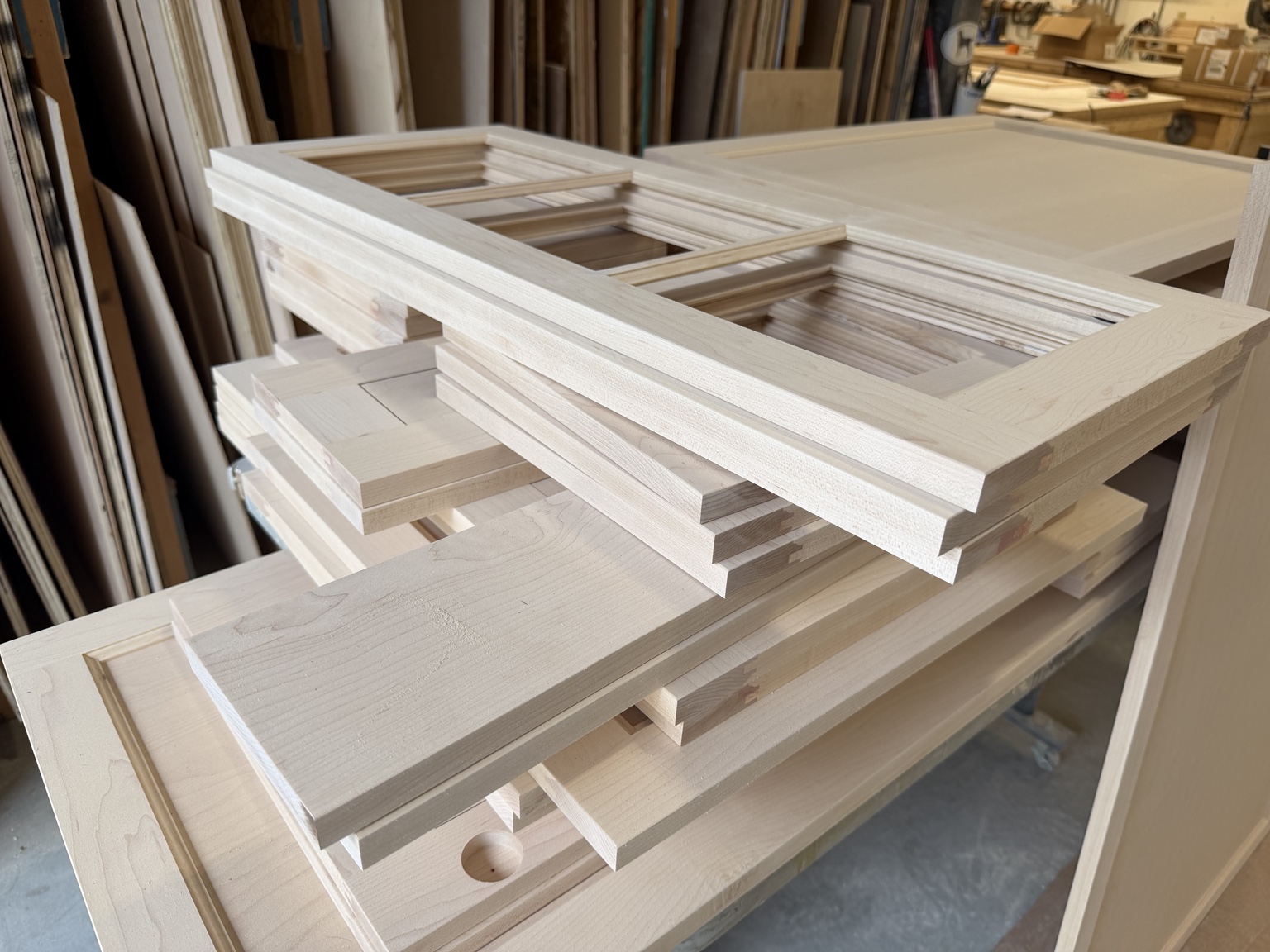 Unfinished wood frames and panels stacked on a bench in the millwork shop