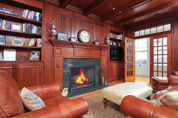 Wood-paneled library with fitted bookcases, a fireplace surround and a detailed wood ceiling