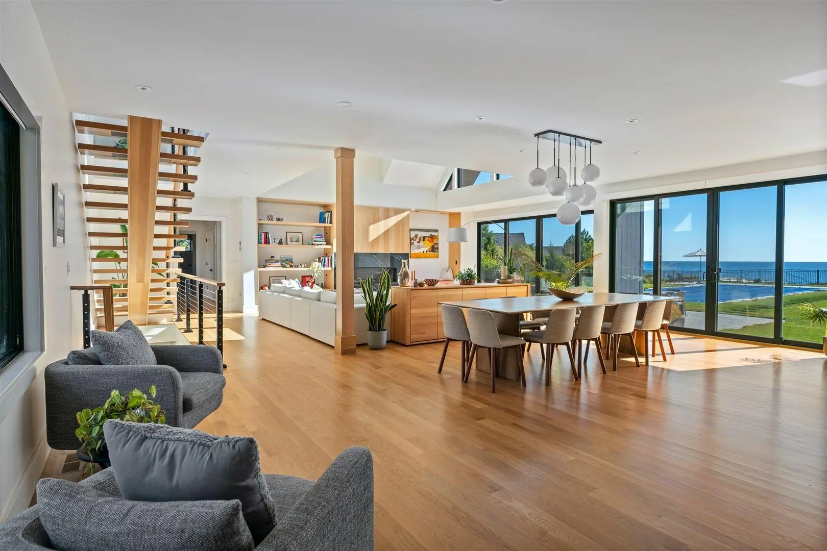 Open living and dining room with a floating wood stair and ocean views through full-height windows