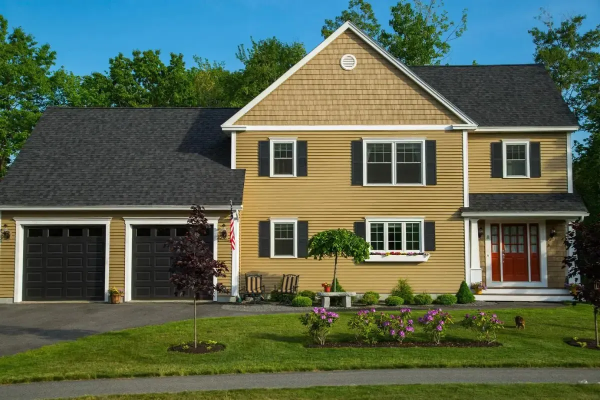 Yellow Colonial with a dark roof and black garage doors