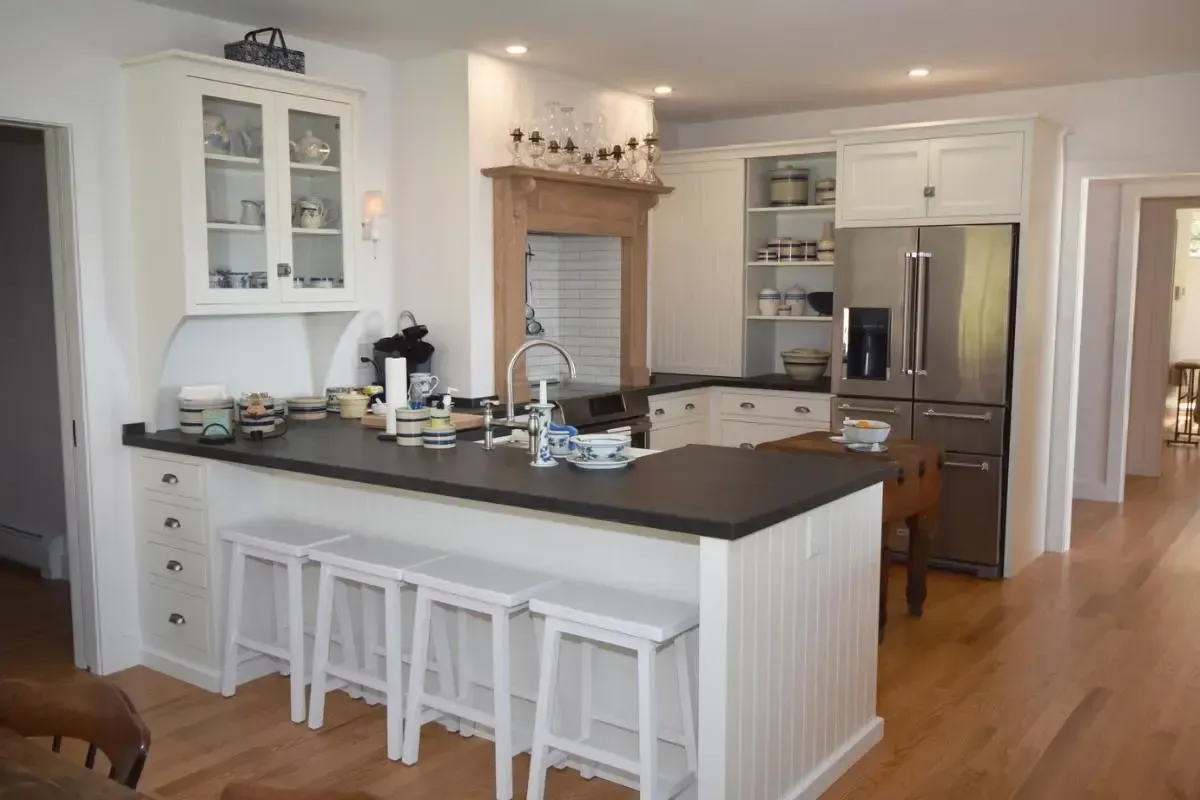 White kitchen with island stools, a refrigerator, and a sink