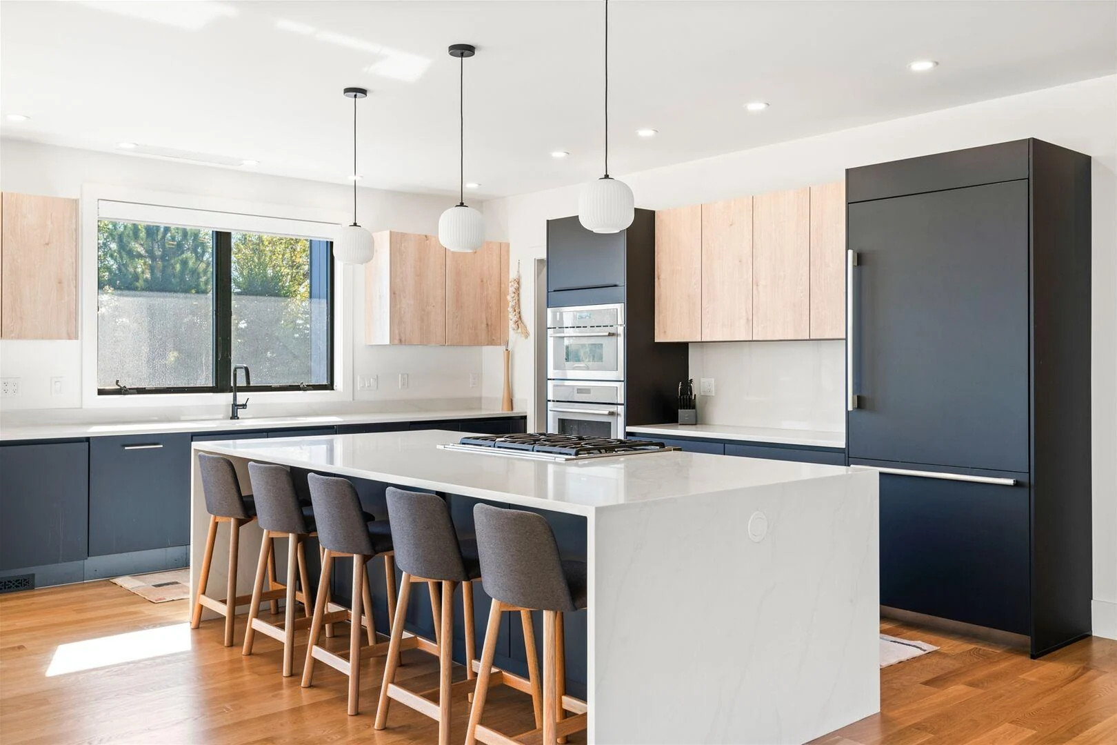 Contemporary kitchen with wood and dark cabinetry, a white island, and globe pendants
