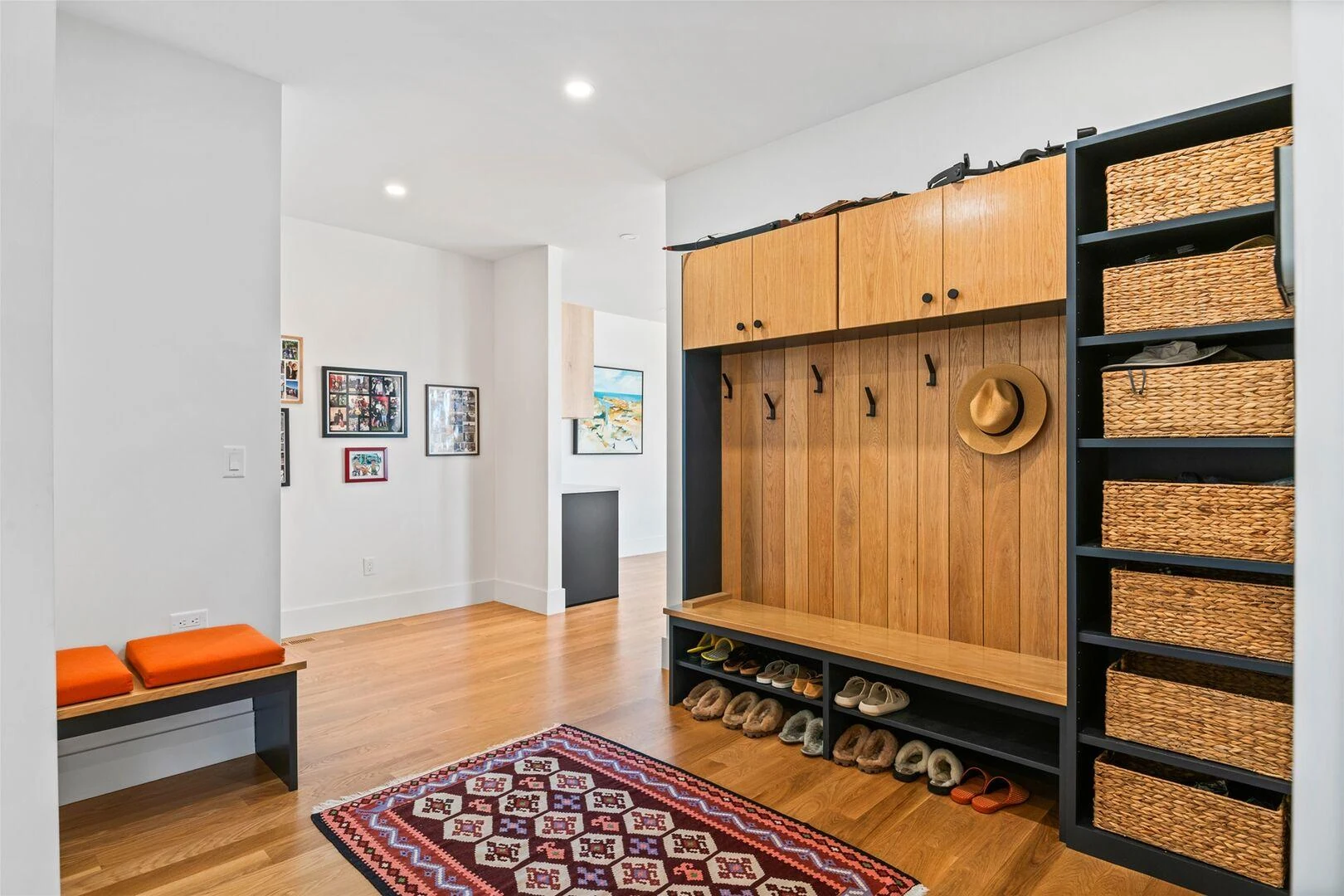 Wood mudroom cabinetry with coat hooks, basket storage, and open shoe shelves
