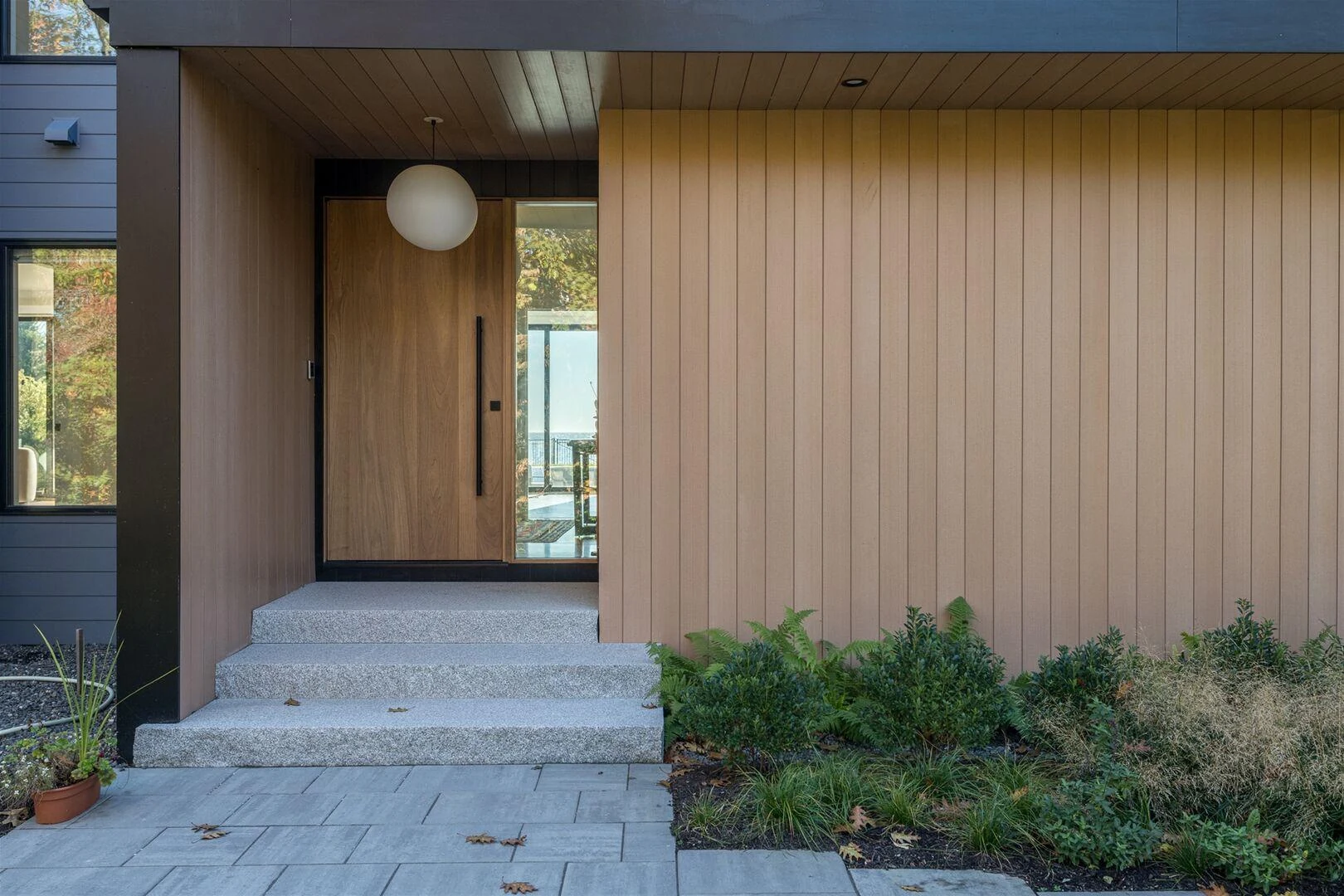 Sheltered wood entrance with a globe pendant, stone steps, and a planted approach