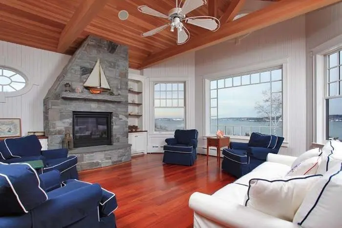 Living room with wood ceiling, stone fireplace, and broad coastal windows