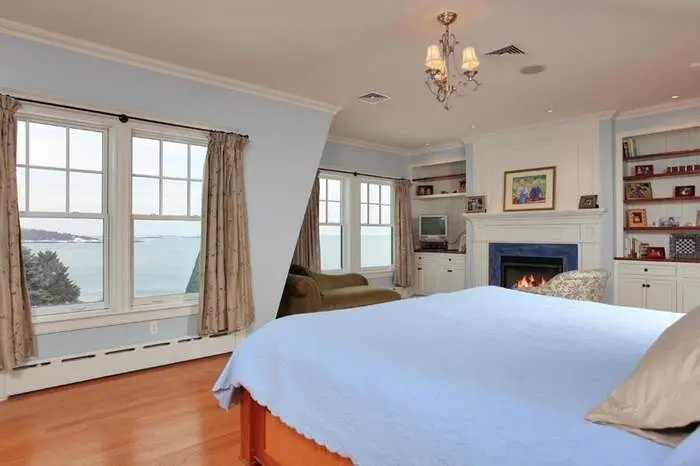 Bedroom and fireplace framed by windows overlooking the water